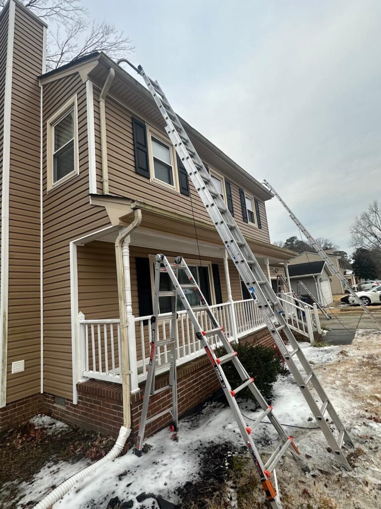 Gutter replacement project setup in Newport News VA with ladders positioned for removal of old sectional gutters