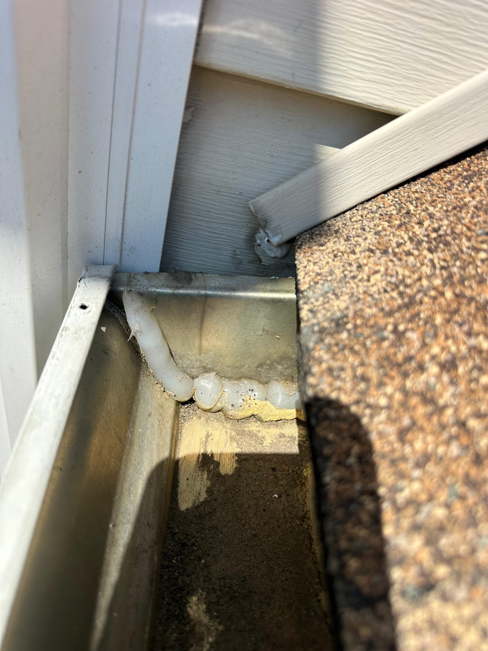 Before: previous installer tried to patch a gap with silicone caulk inside the gutter corner — a clear sign of a cover-up job