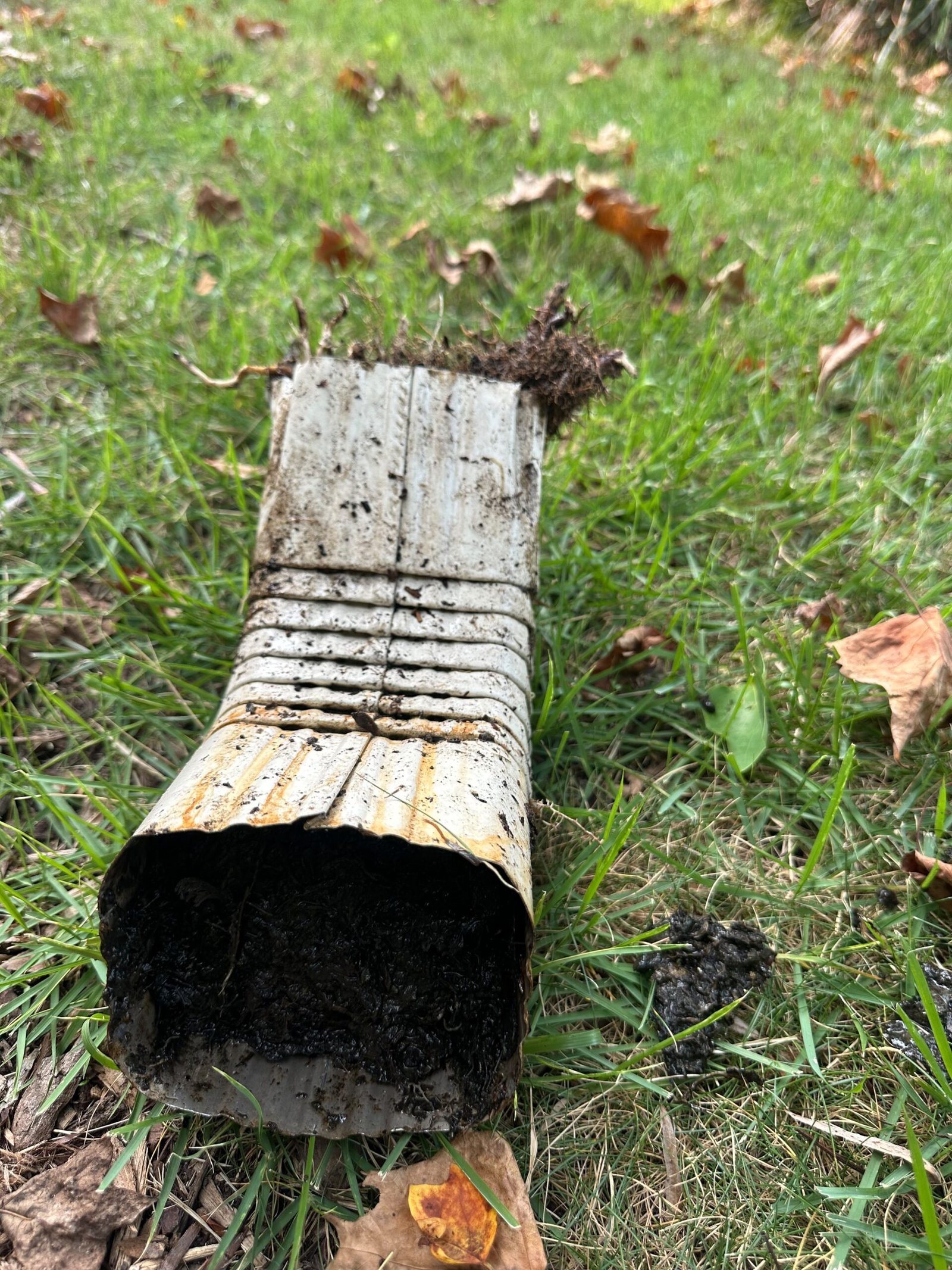 Clogged downspout packed with mud and debris found during a gutter cleaning project in Norfolk, VA.