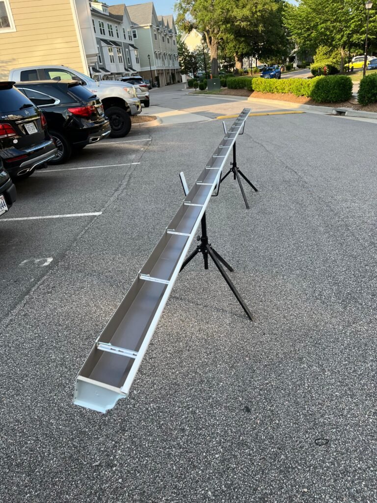 On-site fabrication — Full 200 ft extruded aluminum seamless gutter section formed and propped in the parking lot. Downspout outlet punched, end caps fitted, hidden hanger positioned — all at ground level before the section went up.