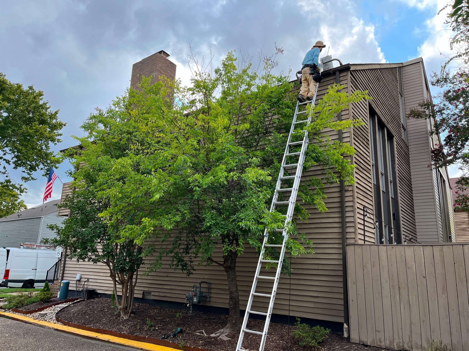 Technician on extension ladder accessing a second-story gutter in Virginia Beach