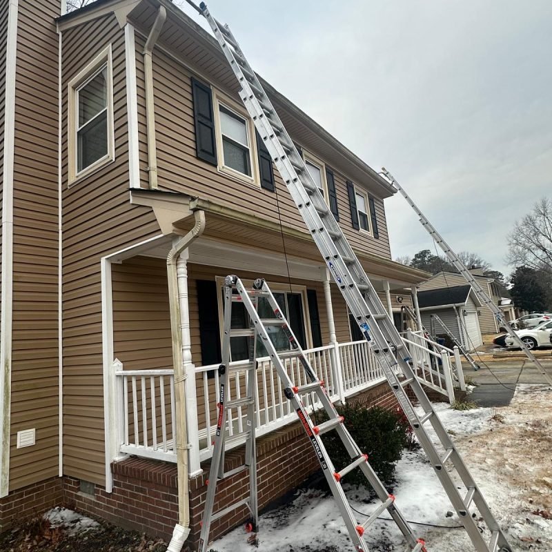 Gutter replacement project setup in Newport News VA with ladders positioned for removal of old sectional gutters
